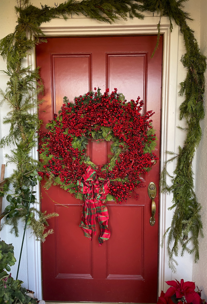 Red Berry holiday wreath displayed on a front door with abundant winter berries, fresh evergreens, and a classic tartan bow.