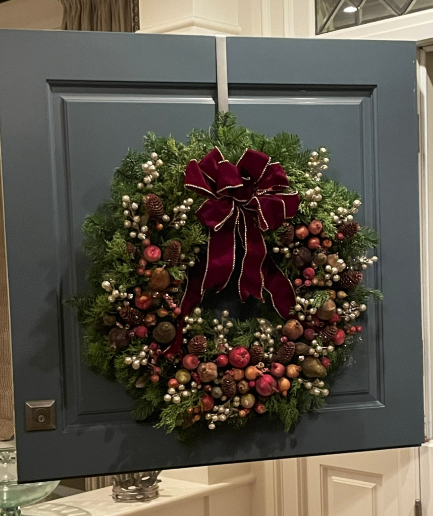 Burgundy Harvest holiday wreath displayed on a front door with seasonal fruit, pinecones, pearl berries, and a burgundy velvet ribbon.