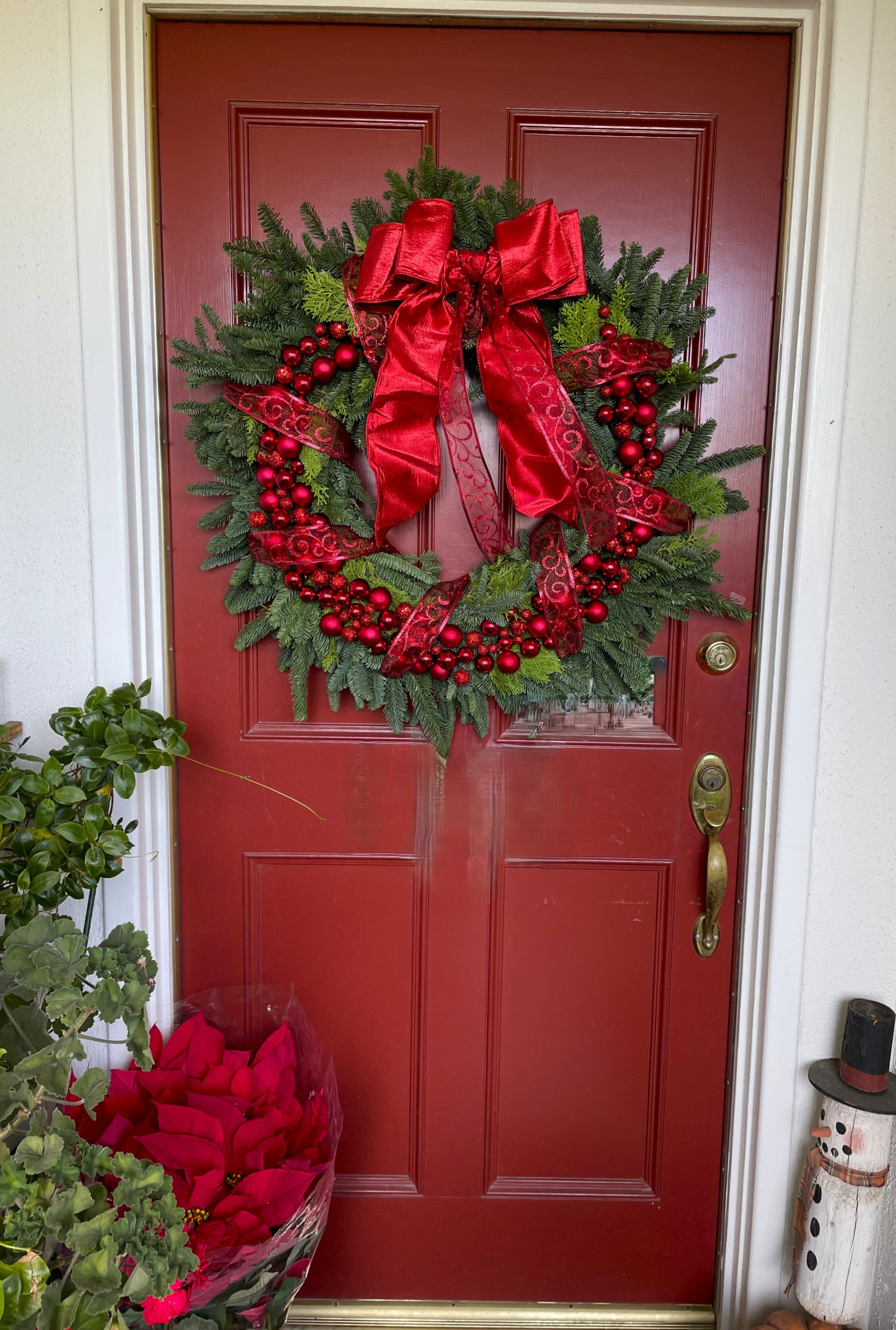 Classic Noël holiday wreath displayed on a front door with fresh evergreens, elegant red ornaments, and a luxurious satin ribbon.