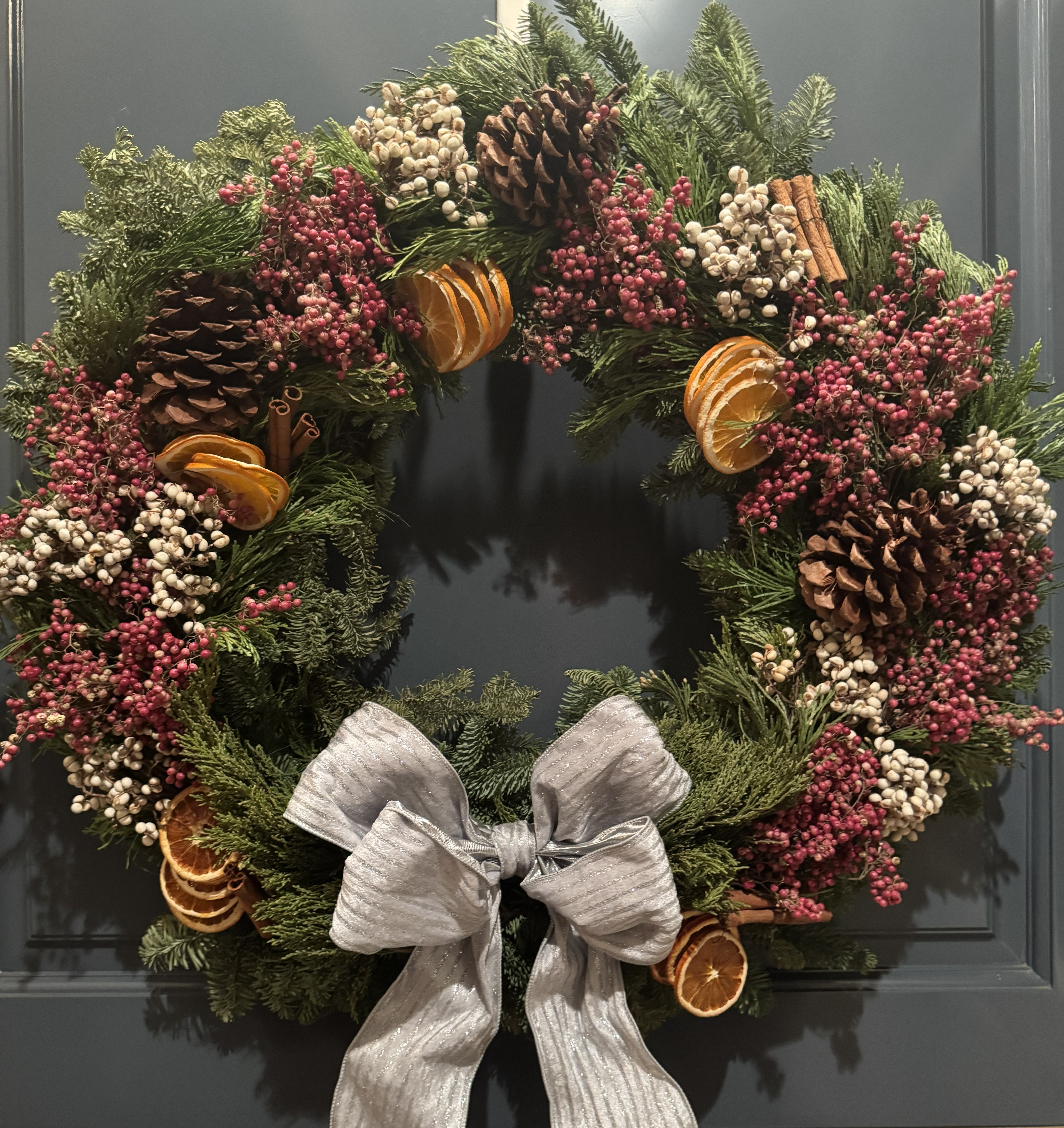 Handcrafted Citrus Grove holiday wreath featuring dried citrus, fresh evergreens, pinecones, winter berries, and a shimmering silver bow.