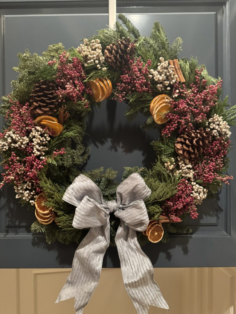Citrus Grove holiday wreath displayed on a front door with dried citrus, fresh evergreens, pinecones, and winter berries.
