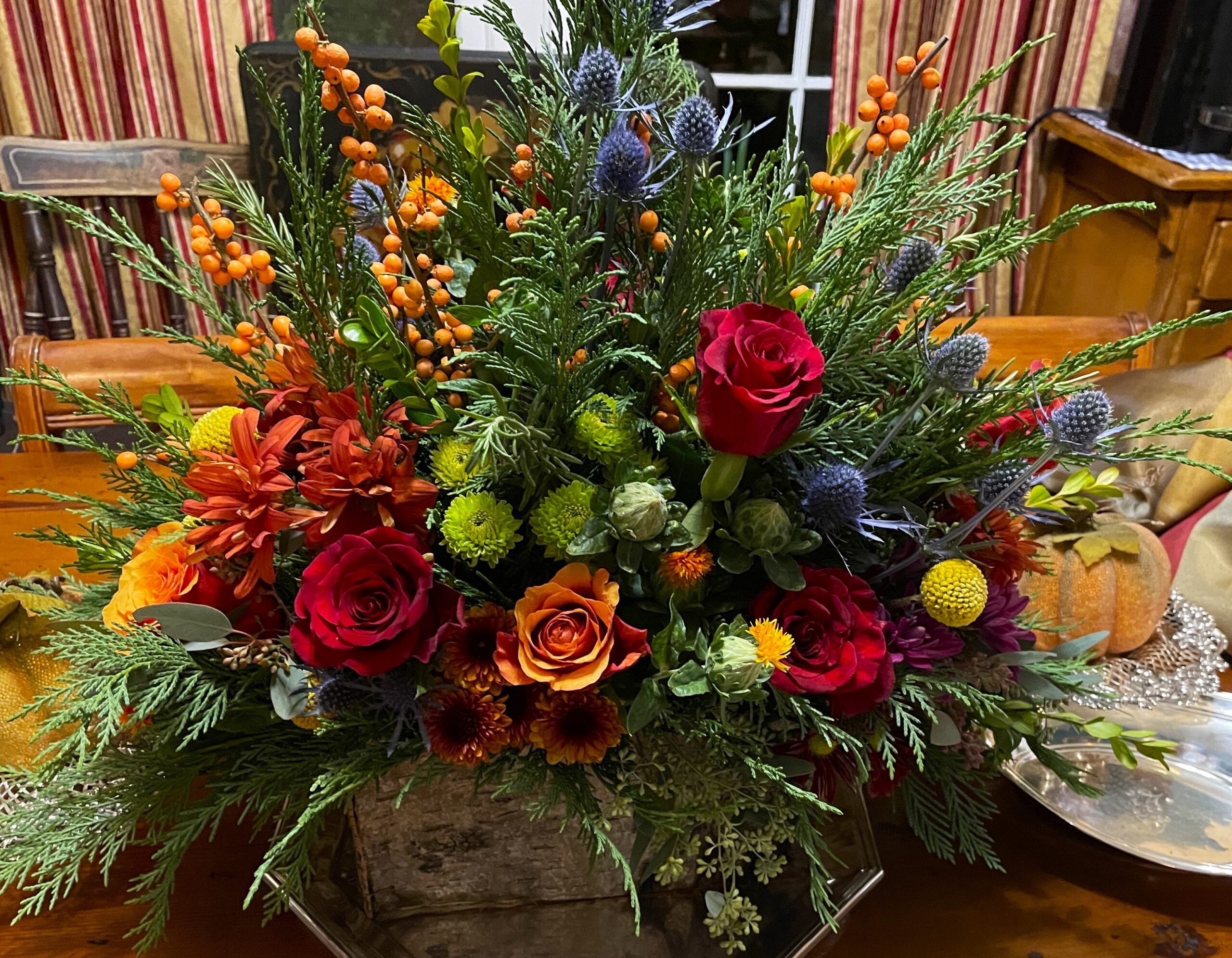 Handcrafted autumn floral centerpiece featuring roses, seasonal blooms, cedar greenery, berries, and textured botanicals.